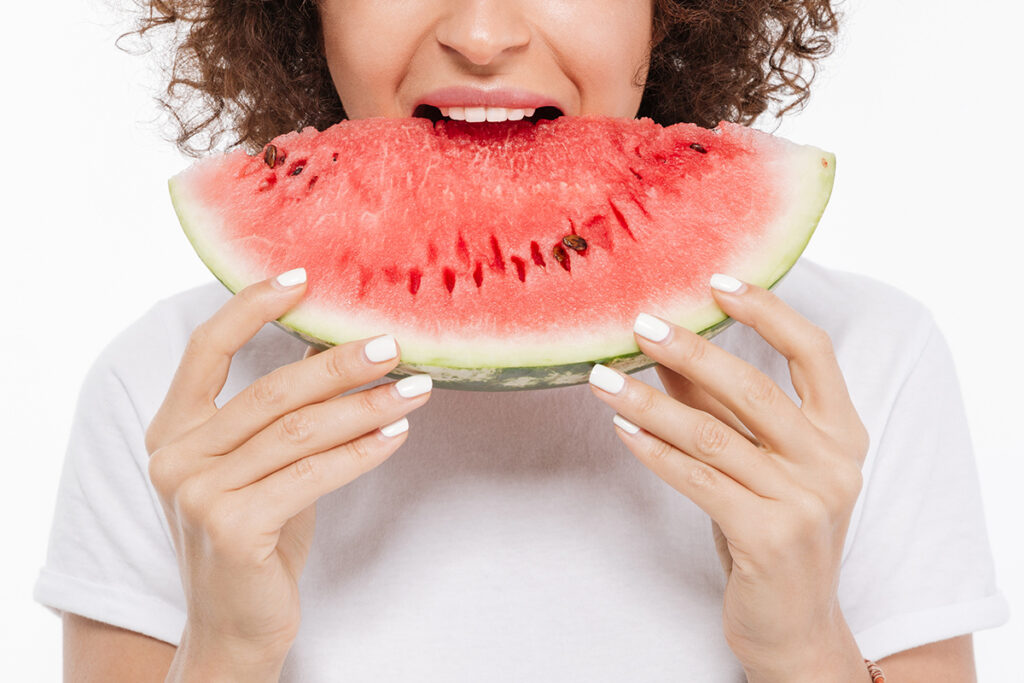 Happy young woman with curly hair eating watermelon.