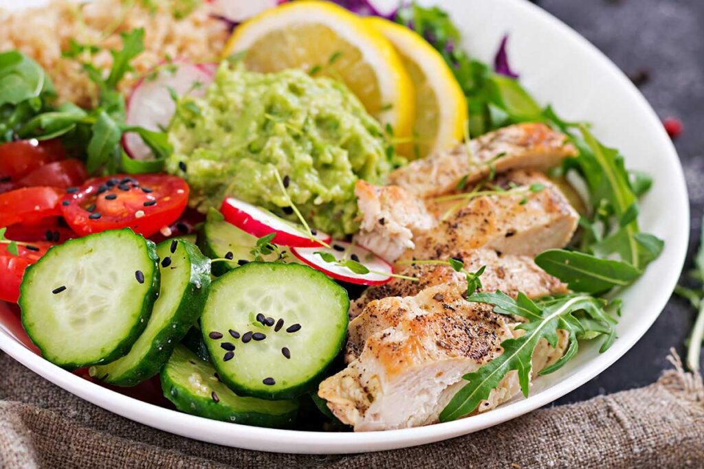 Healthy dinner. Buddha bowl lunch with grilled chicken, tomato, guacamole, red cabbage, cucumber and arugula.