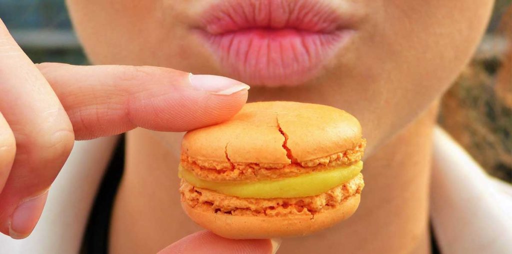 Close-up of woman holding a macaroon to her lips.
