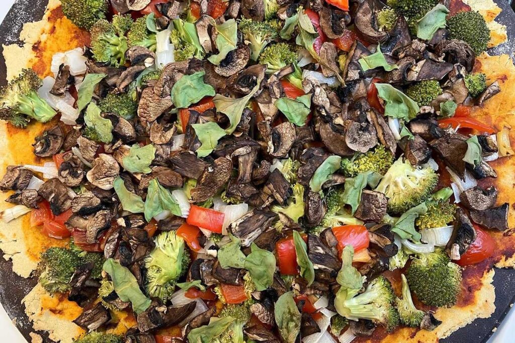 Homemade gluten-free, dairy-free pizza is topped with mushrooms, broccoli, red peppers, onions, and spinach. A healthy, plant-based meal for MS-friendly eating.