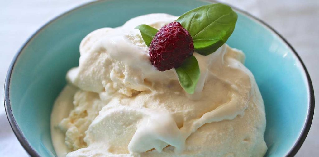 Banana ice cream in blue bowl with raspberry and mint as garnish.