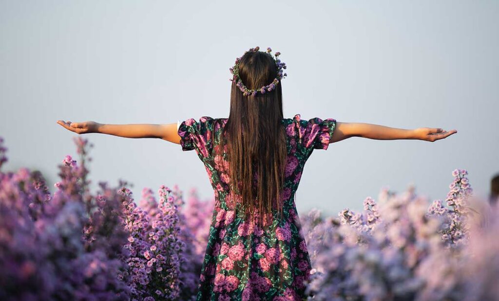 Hippie girl in purple dress among of purple flowers.