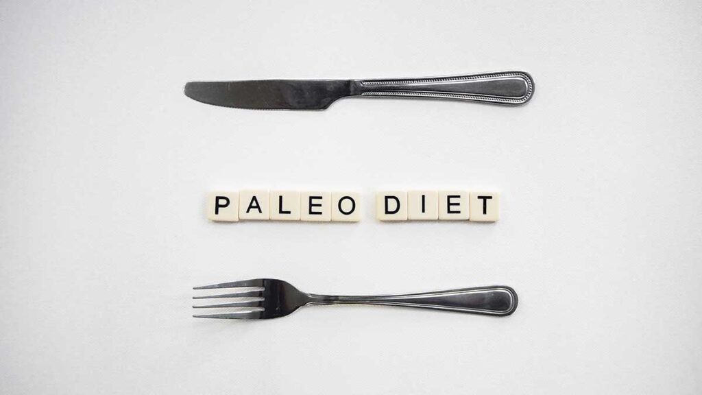 A table knife, Scrabble titles spelling Paleo Diet, and a fork.
