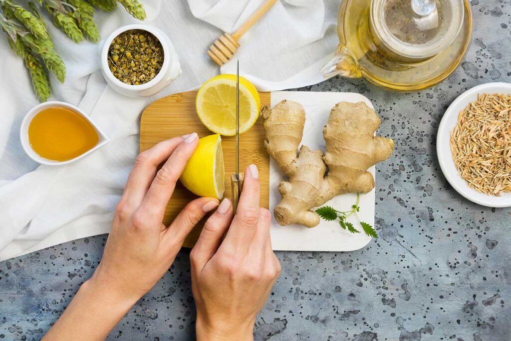 Looking down at a woman cutting a lemon with ginger root and spices nearby.