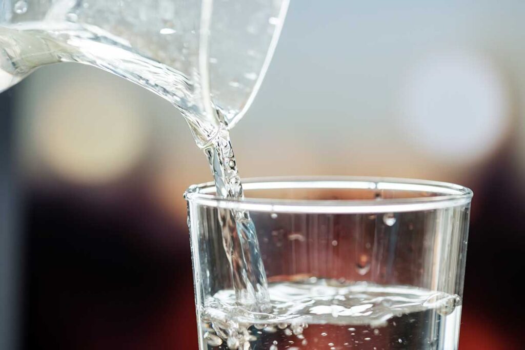 Close up of pitcher pouring water into a glass.