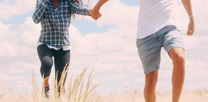 Man and woman holding hands walking through a field.