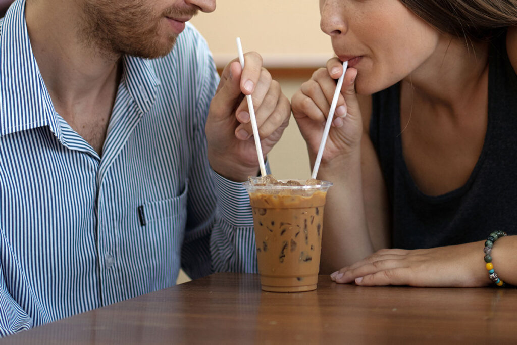 Close up of man and woman sharing a drink with staws.