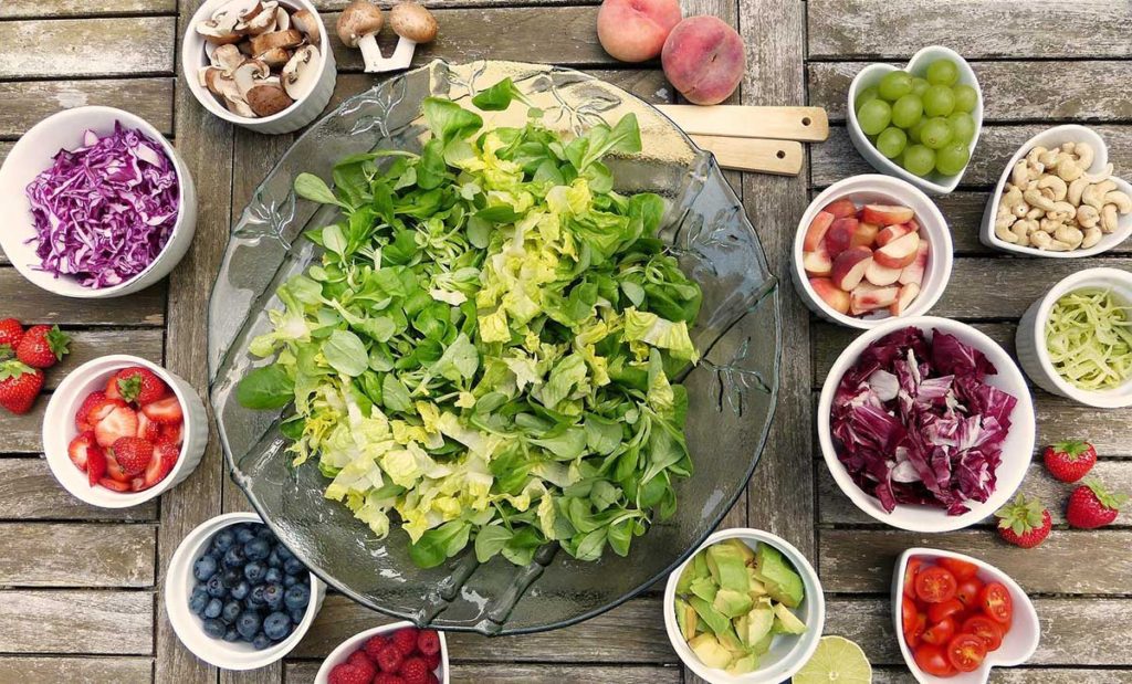 Big glass salad bowl full of lettuce with veggies and fruit on the side.