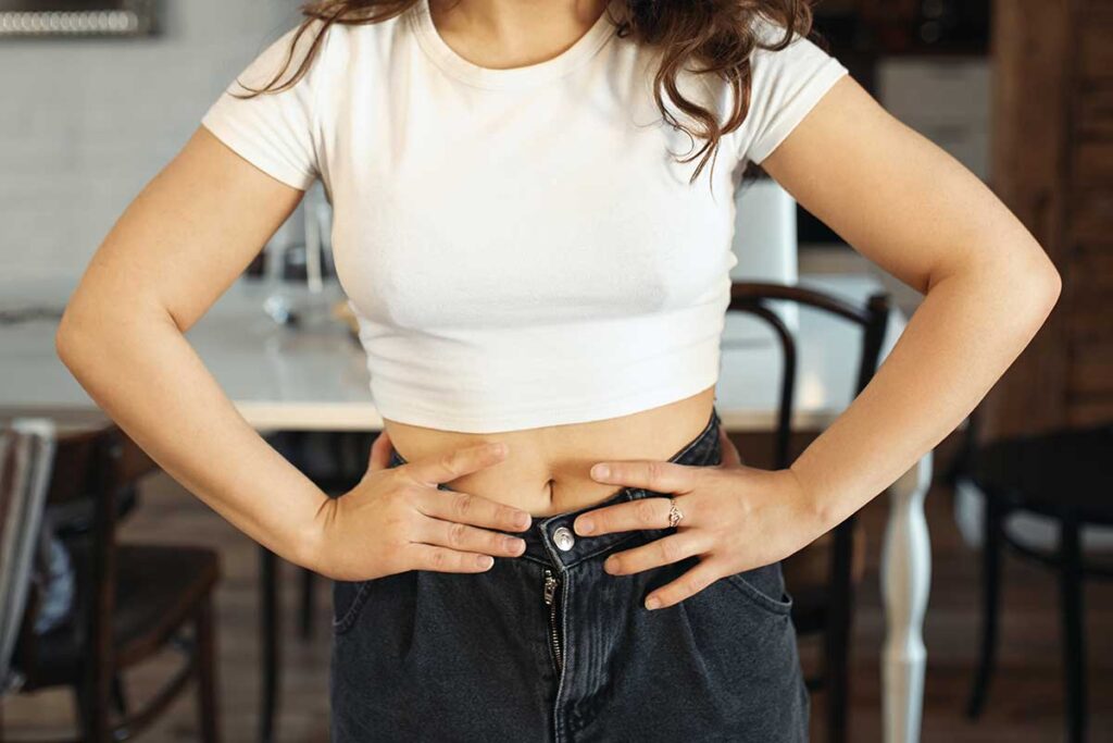 Young woman in jeans and white top holding hands on her waist.