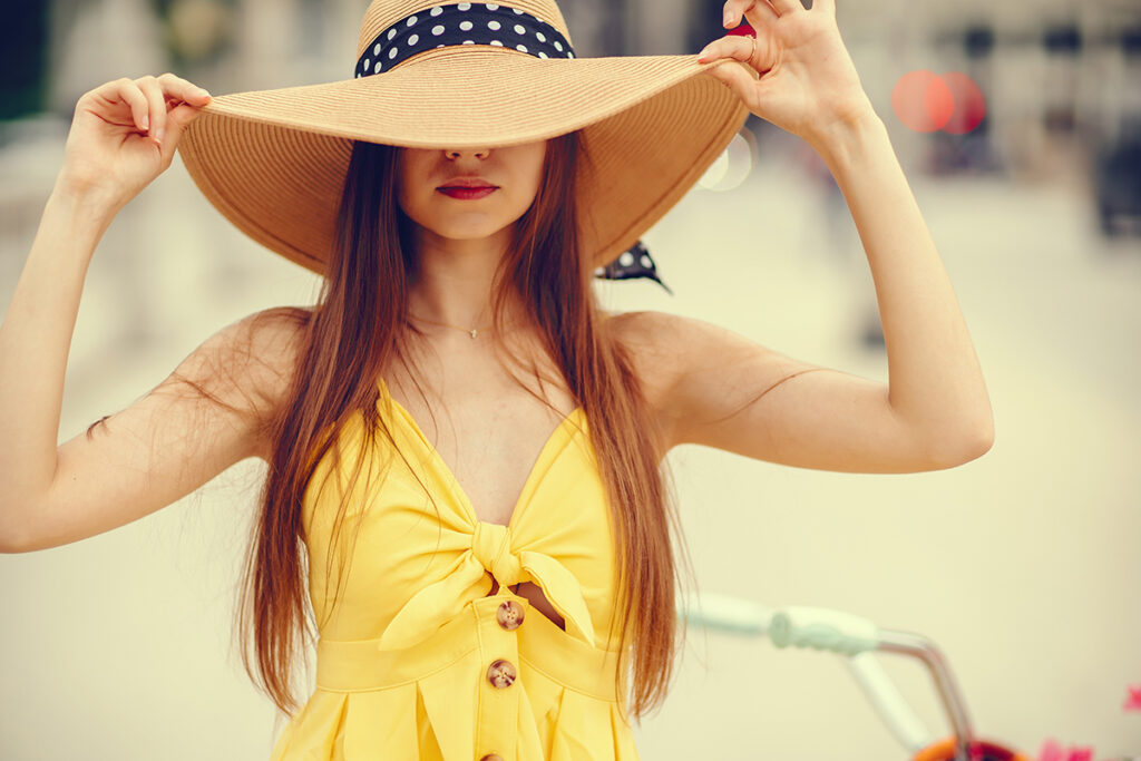 Young red headed woman in yellow wearing a big floppy summer hat.