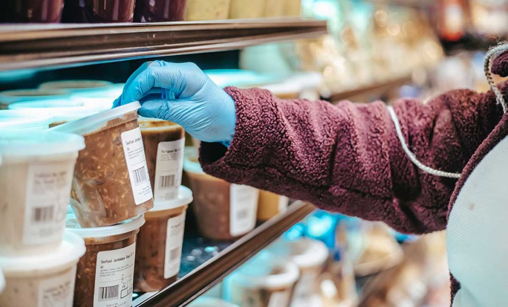 Woman wearing medical gloves reading food label. 