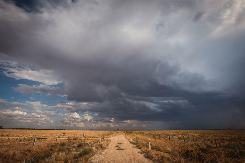 Dirt road going through sagebrush landscape with a dark cloudy sky.