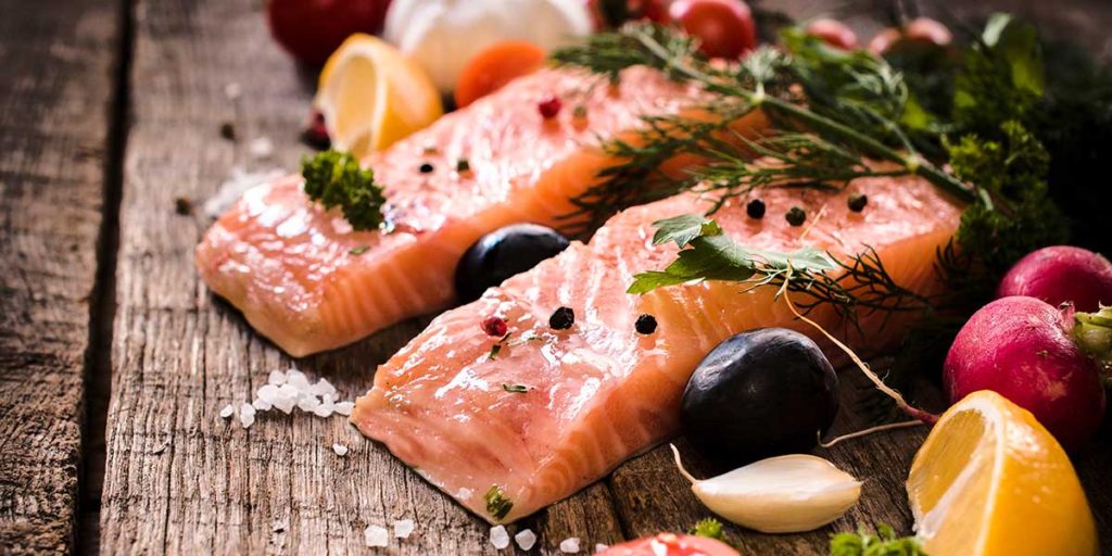 Salmon fillets surrounded by lemon wedges, dill, garlic, and radishes on wooden board.