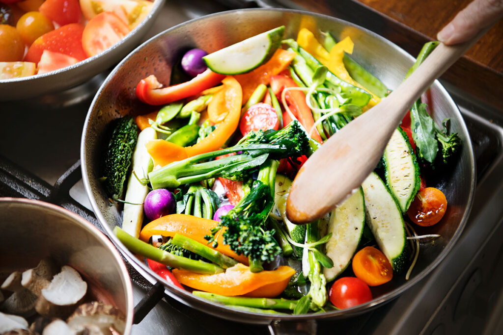 Close up of someone sautéing mixed fresh vegetables.