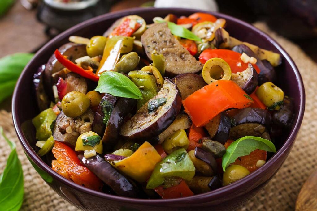 Stew eggplant with sweet pepper , olives, and capers with basil leaves in a bowl.