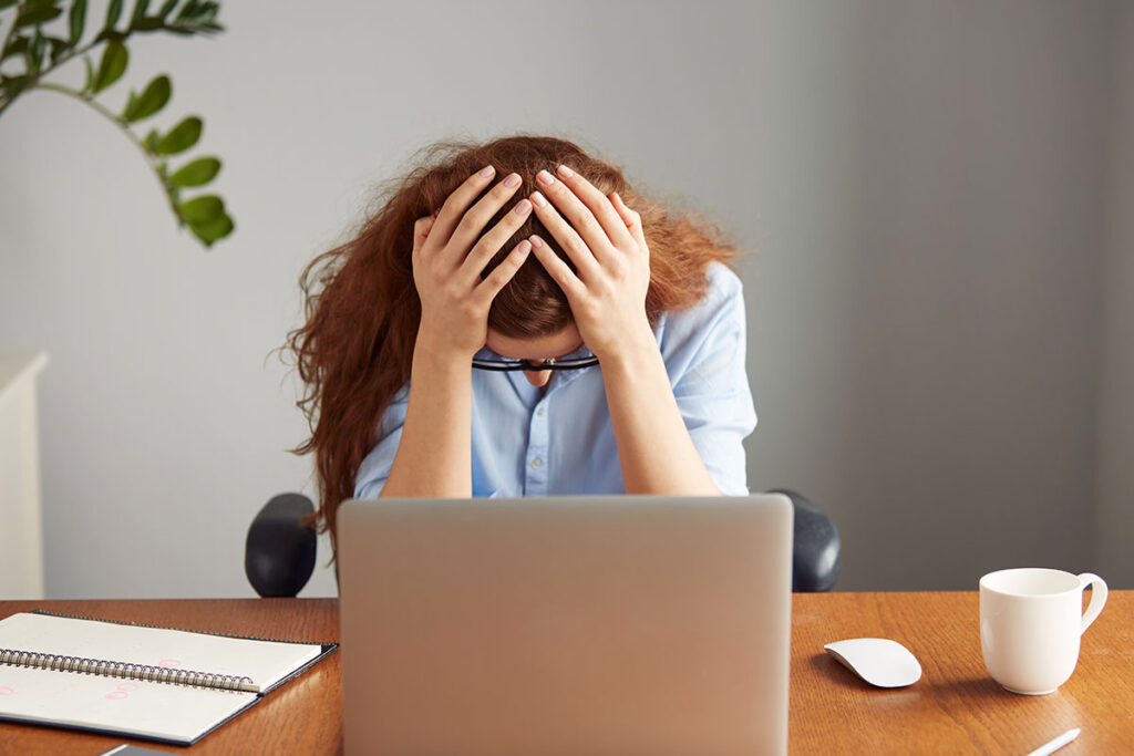 Stressed redhead female office worker in blue shirt hanging her head down.