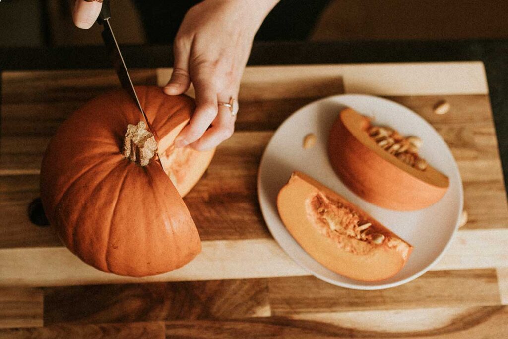 Close up of woman's hands slicing a small pumpkin to eat.