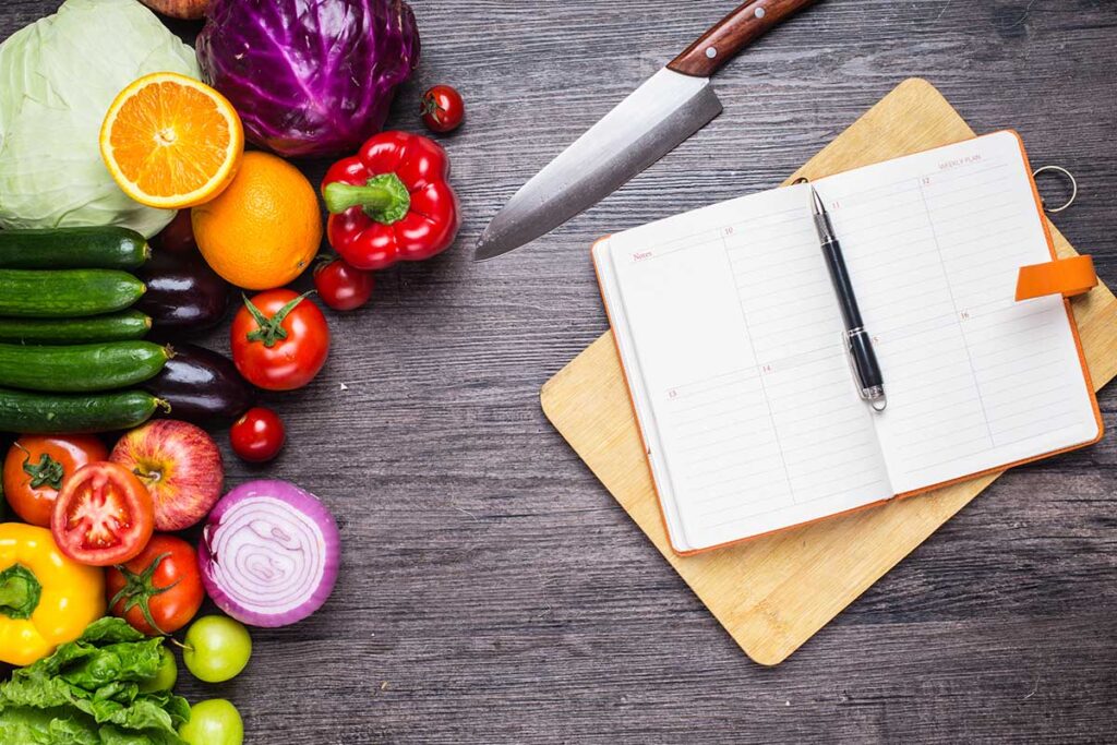 Table with vegetables, a knife and a notebook for meal planning.