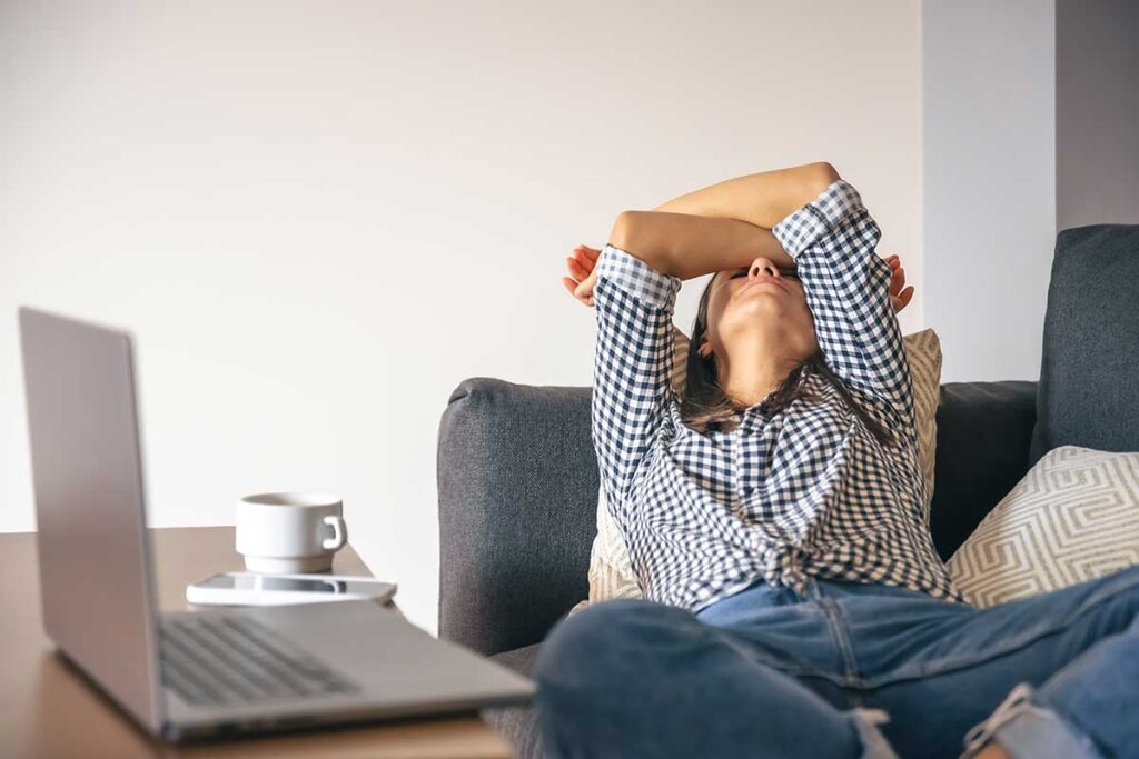 Exhausted young woman in front of a laptop leaning back on sofa.