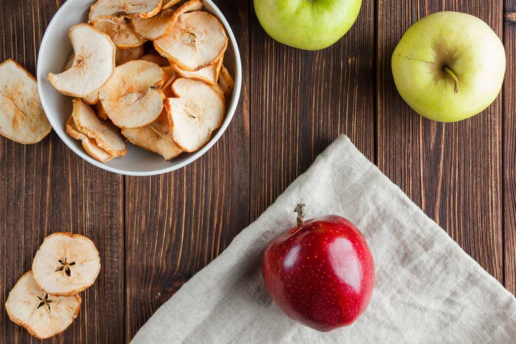 Top view dried apples in bowl with fresh apple on cloth and wooden background.