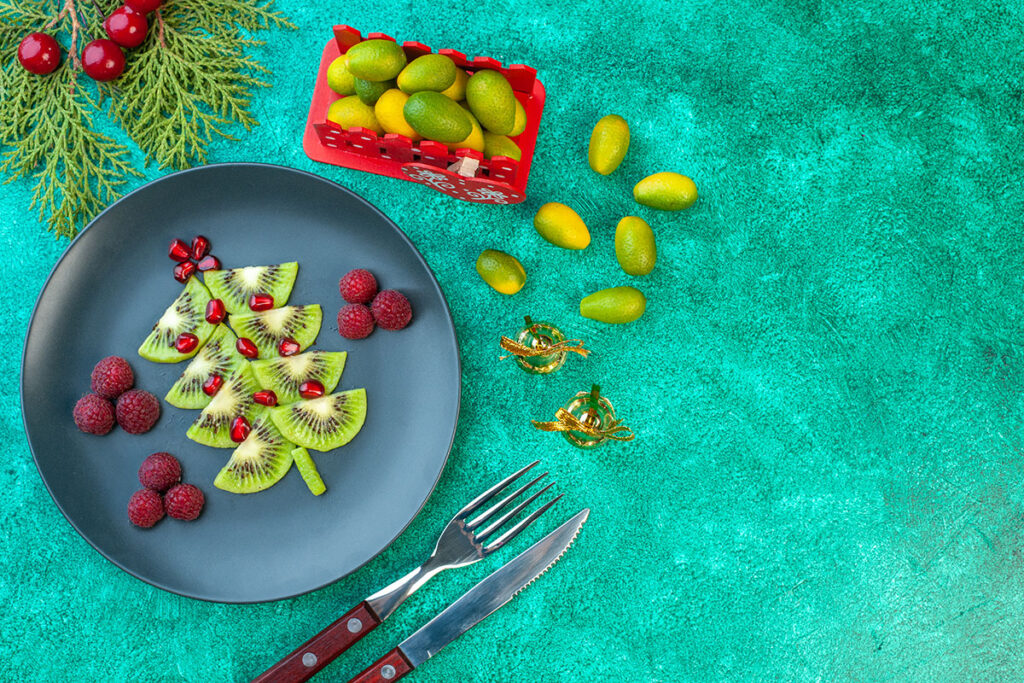 Sliced kiwis on plate in shape of tree with raspberries and cranberries on green background.