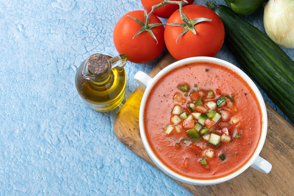 Traditional Spanish gazpacho soup in a bowl on a blue background.