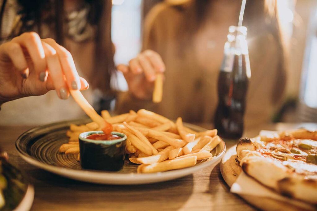 Two women eating fries and pizza with bottle drinks at a restaurant.