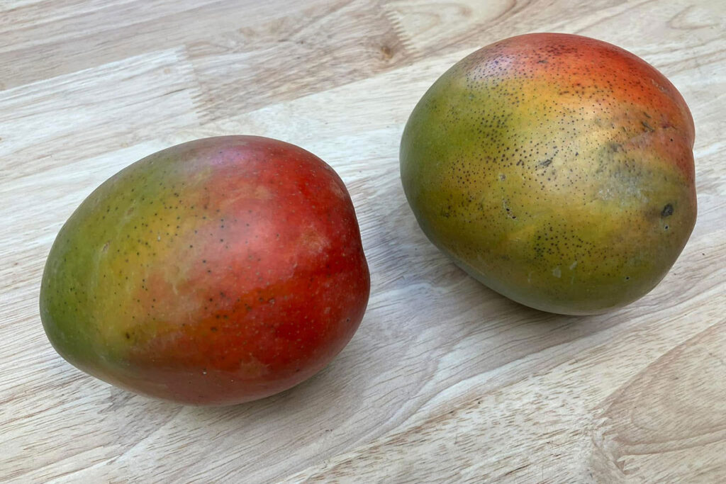 Two mangos on wooden countertop.