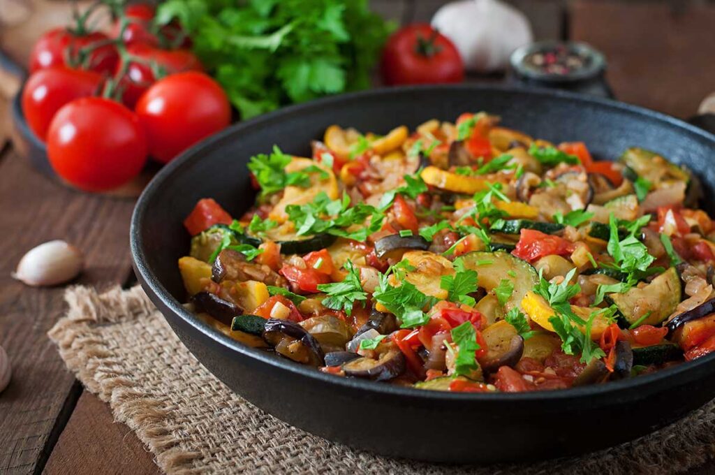 Vegetable ratatouille in a frying pan on a wooden table.