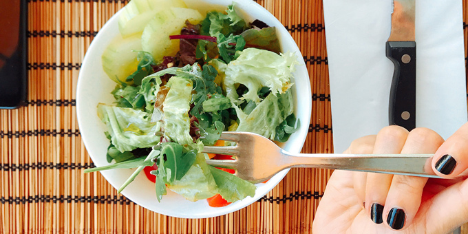 Woman eating a salad from a white bowl.