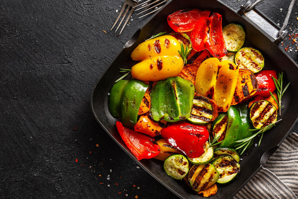 Gilled veggies with herbs in a cast iron pan on dark countertop.