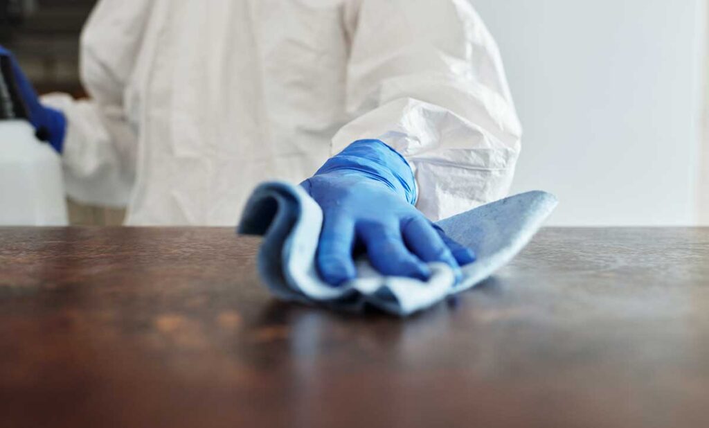 Someone in scrubs wiping down a table with cleaner.