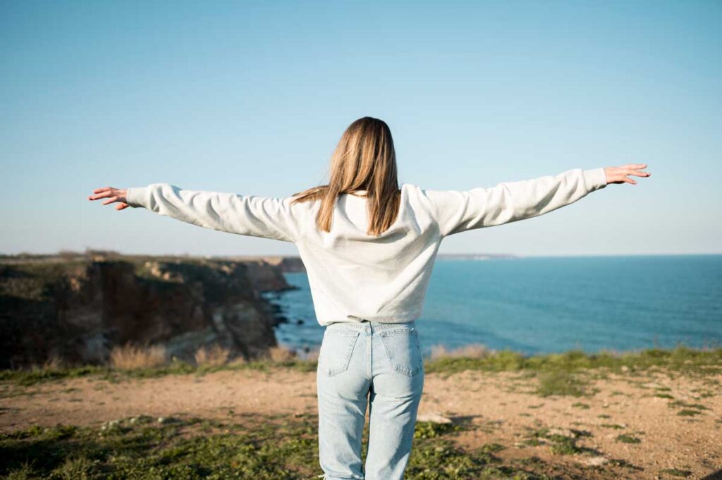 Woman overlooking ocean with arms stretched out.