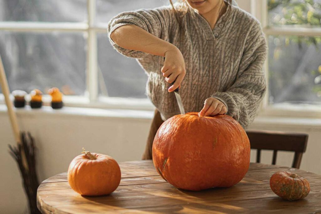 Woman carving pumpkin on small wooden table.