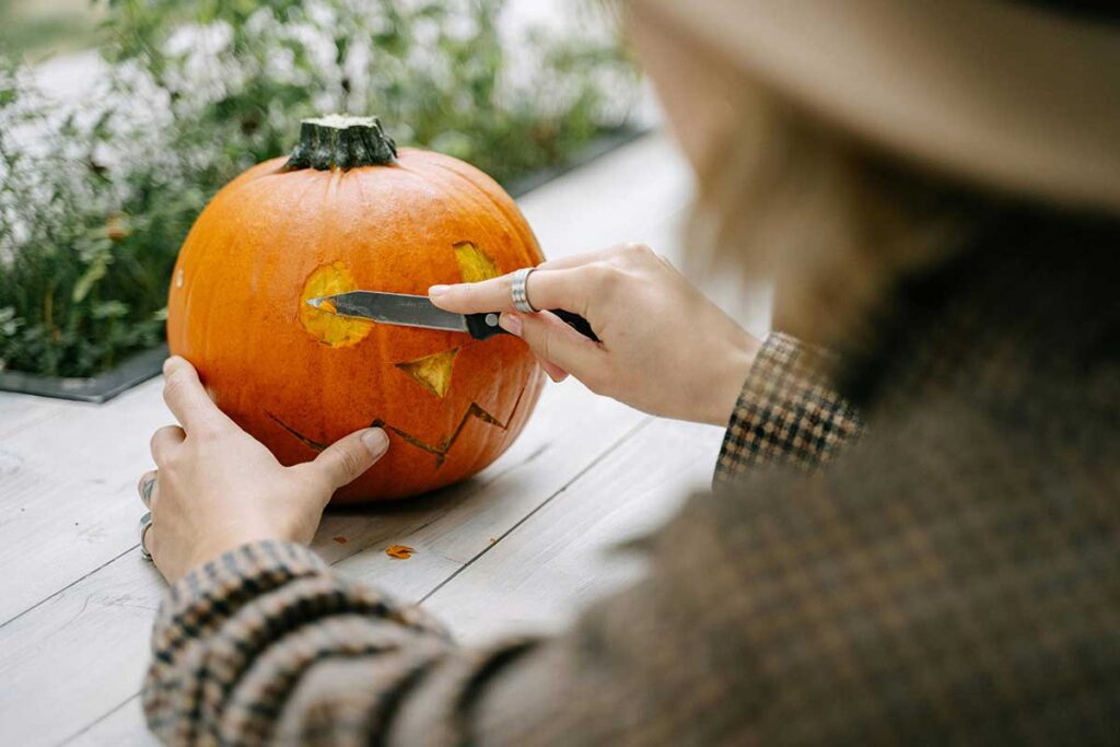 Close up of woman carving a face on a pumpkin.