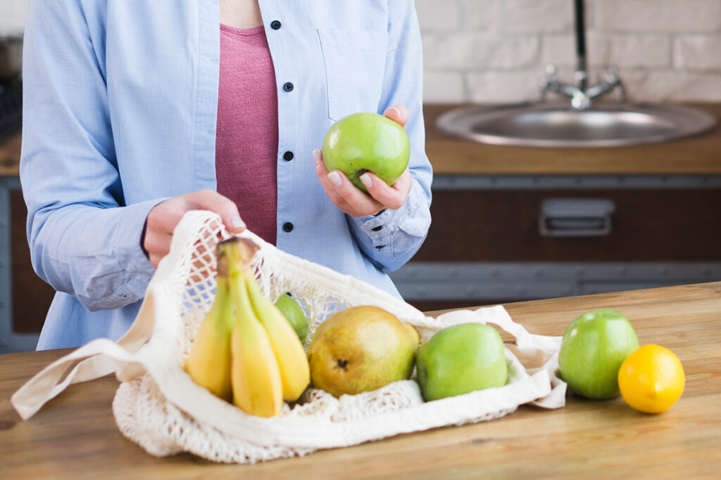 Woman at kitchen counter with cloth grocery bag full of fruit.