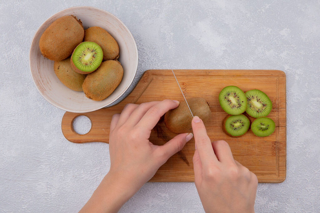 Top view woman cutting kiwi on cutting board and in bowl on white background