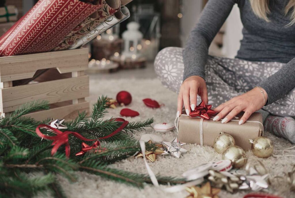 Woman sitting on floor, decorating Christmas present.