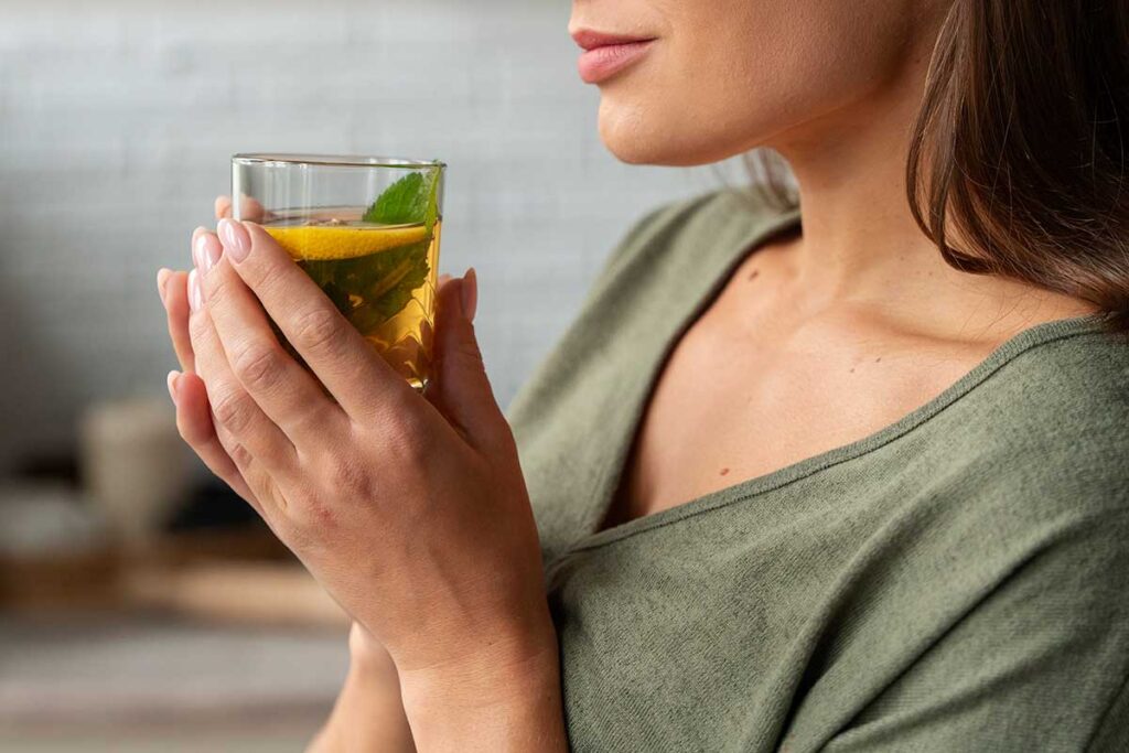 Woman drinking tea with a lemon slice and mint.