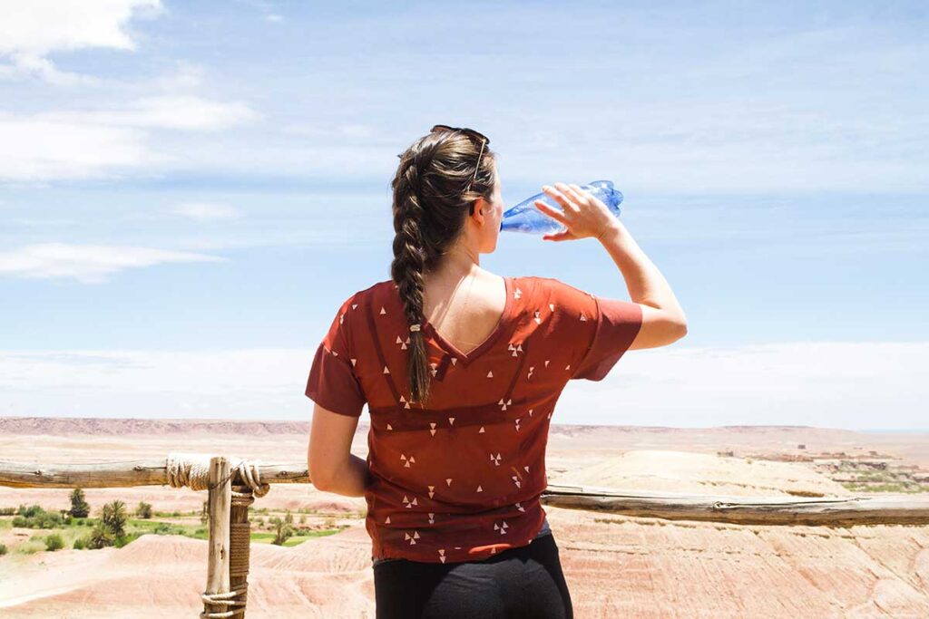 Woman drinking a bottle of water in a dessert oasis.