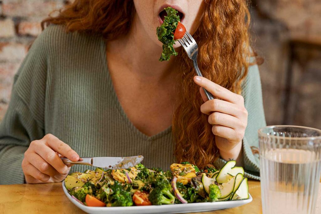 Close up of a red headed woman eating a salad.