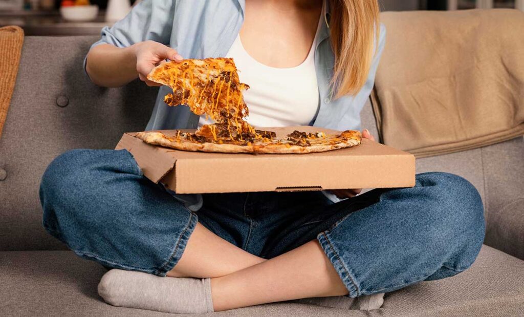 Woman eating pizza while sitting on sofa.