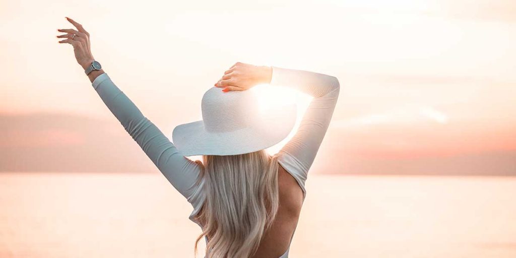 Young woman with left arm in air looking at bright sunshine.