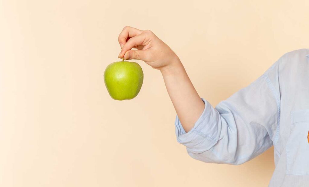 View of woman's arm holding a green apple by the stem.