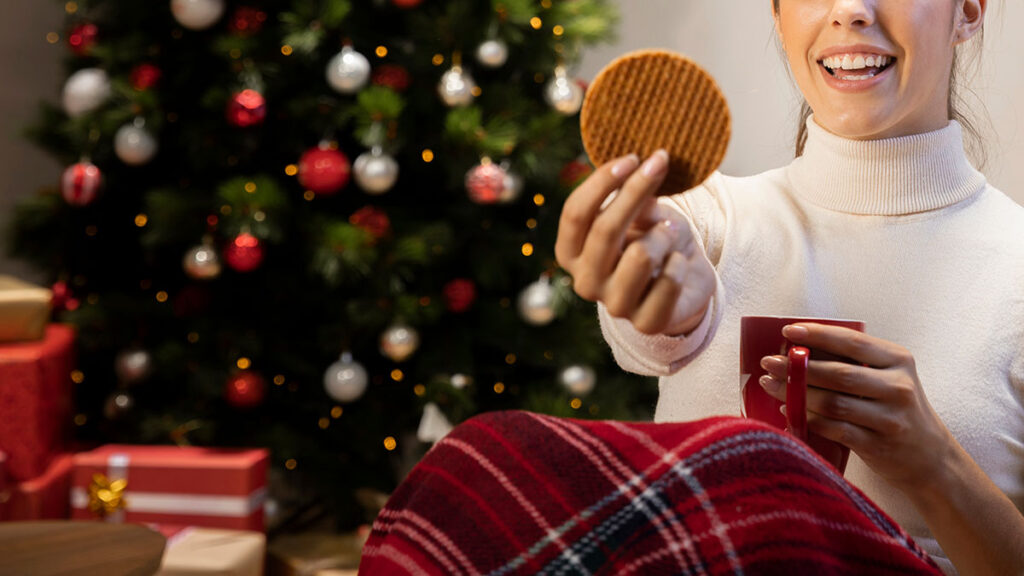 Woman holding cookie and red cup with Christmas tree in background.