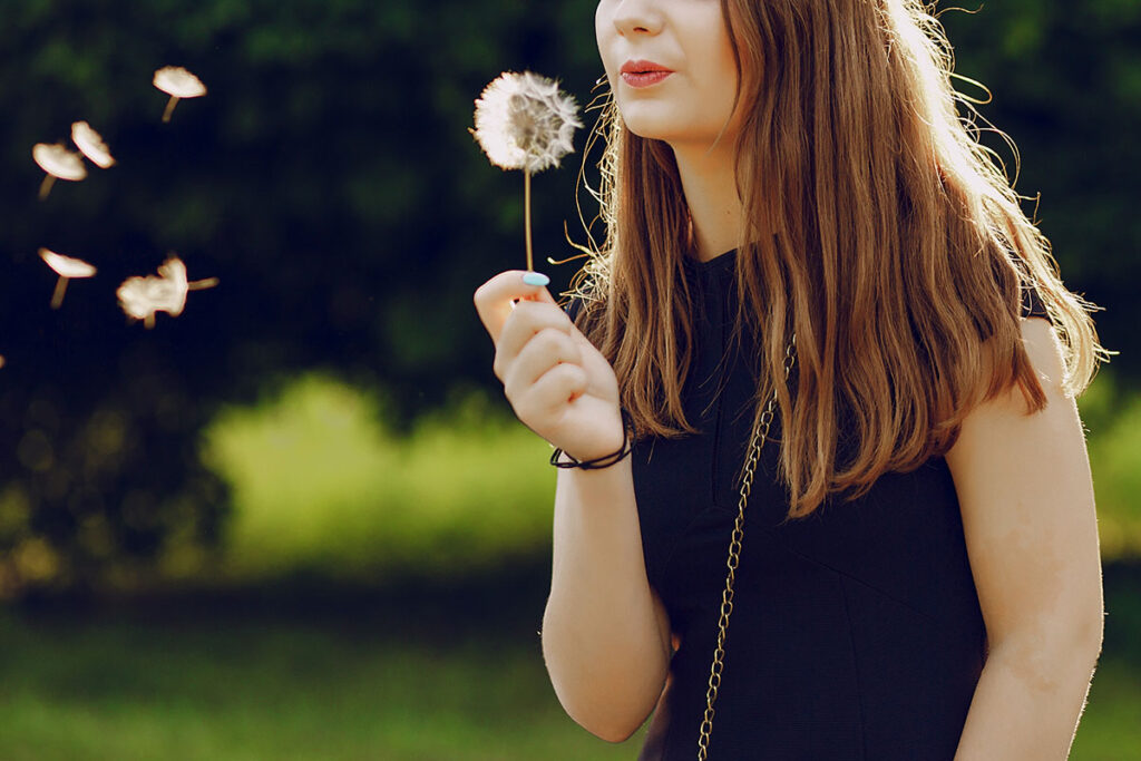 Woman in park blowing dandelion seeds.