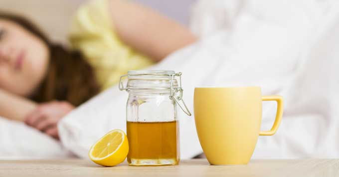 Woman lying in bed not feeling good with a cup of tea and lemon.