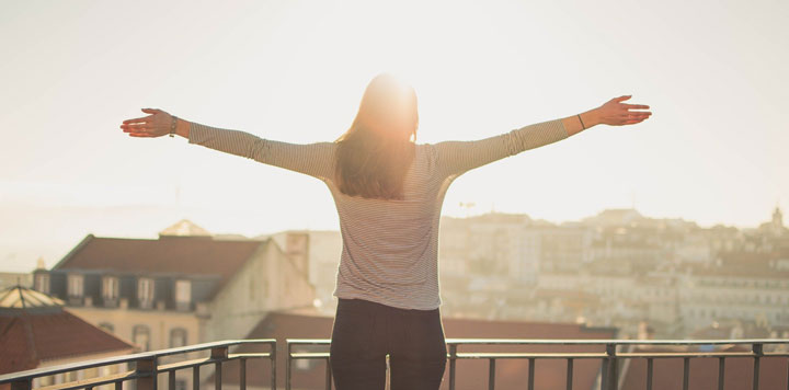 Young woman on balcony with arms stretch out toward the sun.