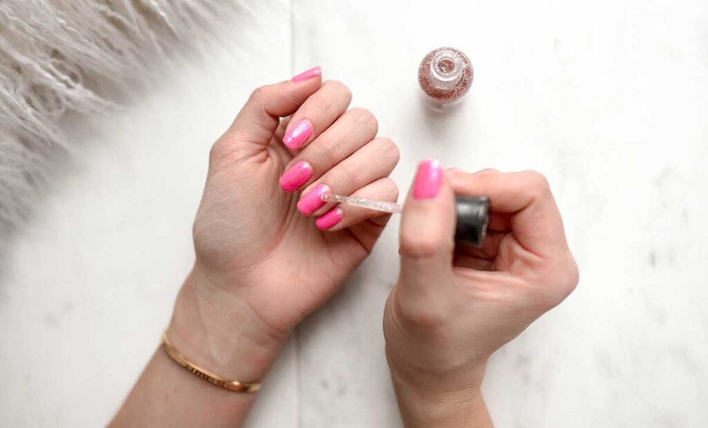 Woman putting on pink nail polish.