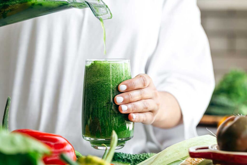 A woman pouring a green smoothie into a glass.